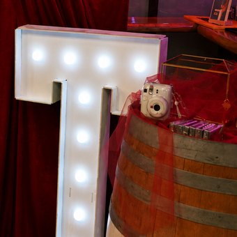 Détail du décor : lettre lumineuse et tonneau avec un appareil instantané
