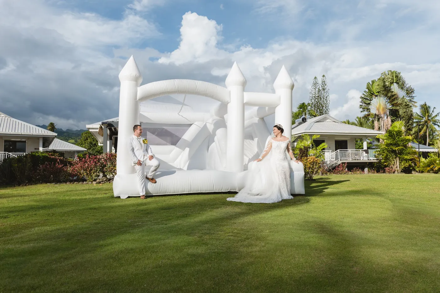 Les mariés posés devant un château gonflable blanc dans un jardin