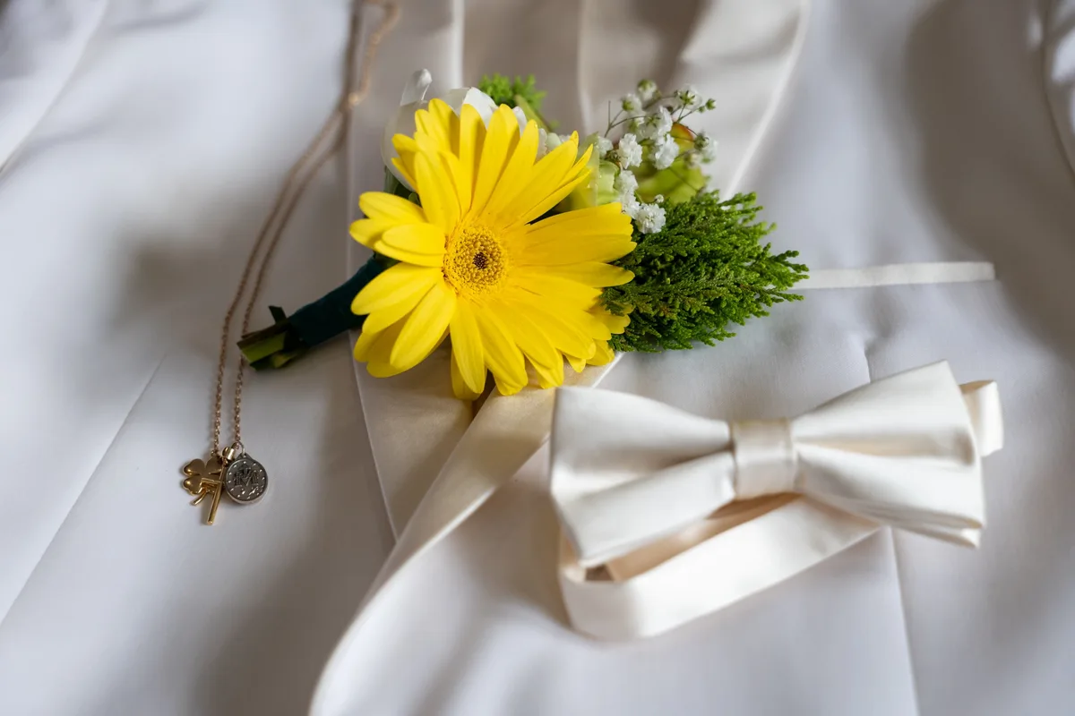 Boutonnière de gerbera jaune, nœud papillon ivoire et collier à trèfle sur un costume blanc