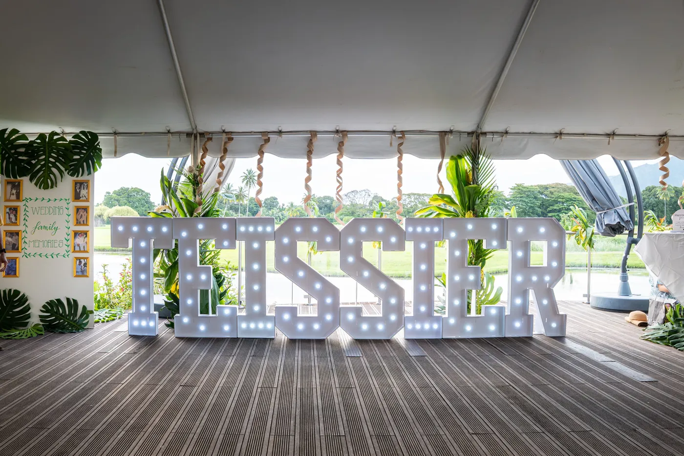 Grandes lettres lumineuses TEISSIER sous une tente décorée de feuillages tropicaux